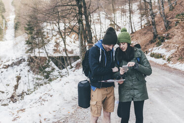 Hiking couple on snowy forest road looking at smartphone, Monte San Primo, Italy - CUF04990
