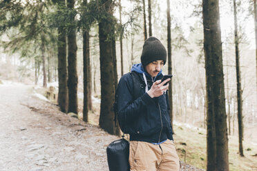 Junger männlicher Wanderer schaut im Wald auf sein Smartphone, Monte San Primo, Italien - CUF04993