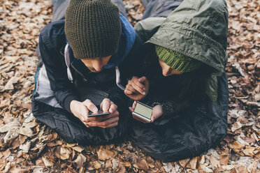 Wanderndes Paar in Schlafsäcken liegend und mit Blick auf Smartphones im Wald, Monte San Primo, Italien - CUF04997