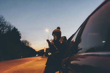 Woman looking at smartphone on roadside at dusk, Monte San Primo, Italy - CUF05007