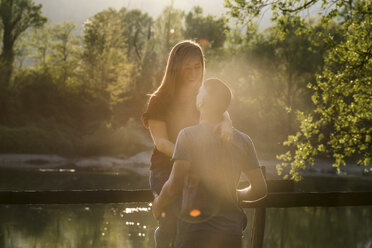 Couple beside river, young woman sitting on fence, facing young man, smiling - CUF05008