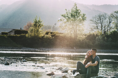 Romantic couple sitting on rocks beside river, smiling - CUF05013