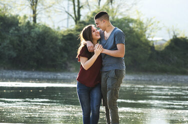 Romantic couple standing beside river, face to face, smiling - CUF05014