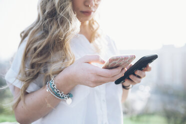 Young woman outdoors, looking at two smartphones, mid section - CUF05027