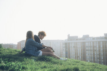 Young couple sitting on grassy verge overlooking rooftops - CUF05028