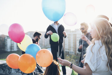 Eine Gruppe von Freunden genießt eine Dachparty, eine junge Frau hält Heliumballons - CUF05043