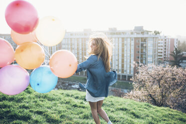 Young woman standing on roof, holding helium balloons - CUF05044