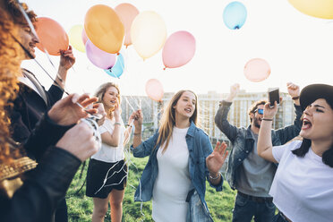 Group of friends enjoying roof party, holding helium balloons - CUF05047