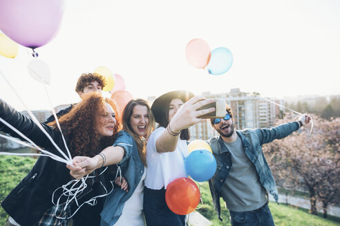 Eine Gruppe von Freunden genießt eine Dachparty, hält Heliumballons, eine junge Frau macht ein Selfie mit ihrem Smartphone - CUF05048