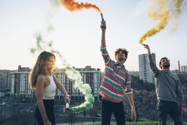 Group of friends on roof, holding colourful smoke flares - CUF05051