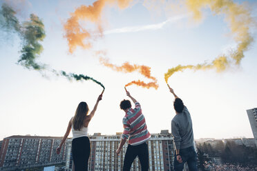 Group of friends on roof, holding colourful smoke flares, rear view - CUF05052