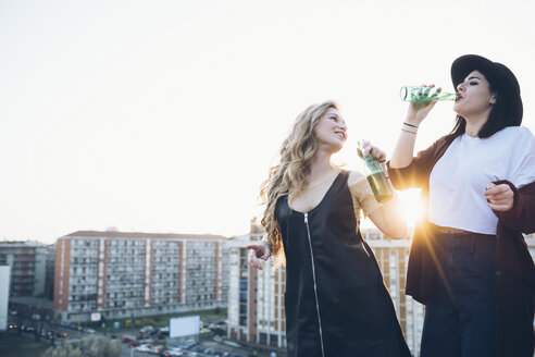 Zwei junge Frauen auf einem Dach, die Bier aus Flaschen trinken - CUF05054