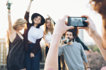 Group of friends enjoying roof party, young man taking photograph using smartphone - CUF05058