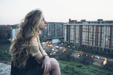 Junge Frau auf dem Dach sitzend, mit nachdenklichem Gesichtsausdruck - CUF05068