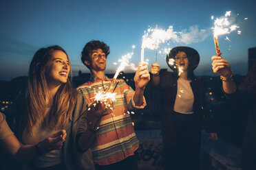 Group of friends enjoying roof party, holding lit sparklers - CUF05072
