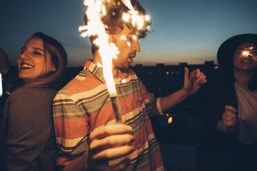 Group of friends enjoying roof party, holding lit sparklers - CUF05073