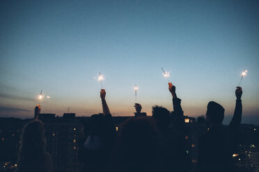 Group of friends enjoying roof party, holding lit sparklers in air, rear view - CUF05076