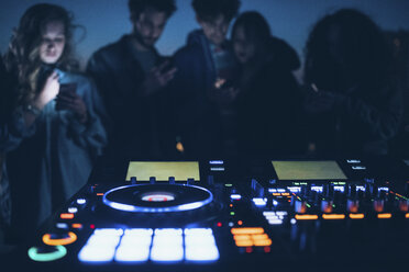 Group of people at roof party, standing around illuminated mixing desks - CUF05077