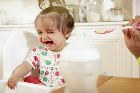 Ein weinendes Mädchen, das von seiner Mutter mit Frühstück gefüttert wird - CUF05078