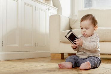 Kleiner Junge sitzt auf dem Boden und schaut auf sein Smartphone - CUF05087