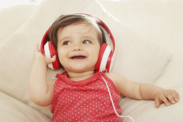 Baby girl on sofa listening to red headphones - CUF05096