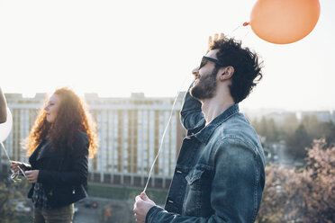 Friends standing on roof, holding helium balloons - CUF05114