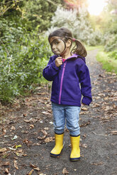 Porträt eines jungen Mädchens auf einem ländlichen Weg, das durch ein Vergrößerungsglas schaut - CUF05118