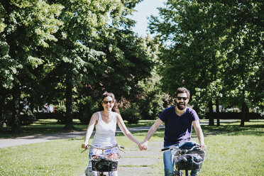 Paar hält sich beim Radfahren im Park an den Händen, Arezzo, Toskana, Italien - CUF05141