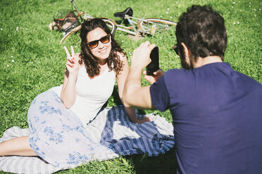 Over shoulder view of man photographing girlfriend sitting in park, Arezzo, Tuscany, Italy - CUF05146