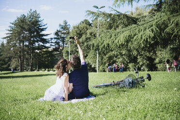 Rückansicht eines Paares, das im Park sitzend ein Smartphone-Selfie macht, Arezzo, Toskana, Italien - CUF05147