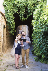 Paar mit digitalem Tablet, das von einer gepflasterten Straße aufblickt, Arezzo, Toskana, Italien - CUF05150