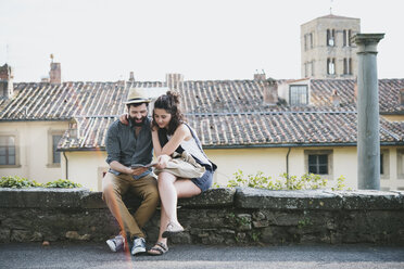 Couple sitting on wall looking at guidebook, Arezzo, Tuscany, Italy - CUF05151