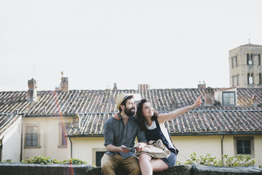 Paar sitzt auf einer Mauer und zeigt auf sie, Arezzo, Toskana, Italien - CUF05152