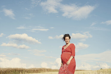 Porträt einer schwangeren Frau in einem Weizenfeld vor blauem Himmel - CUF05164