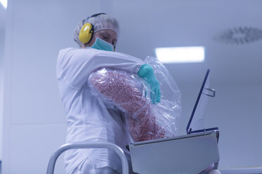 Arbeiter, der in einer pharmazeutischen Fabrik Tabletten in eine Sortiermaschine gibt - CUF05207