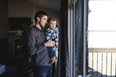 Man and toddler son looking at of window at home - CUF05222