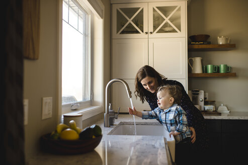 Mother helping toddler son wash hands at kitchen sink - CUF05230