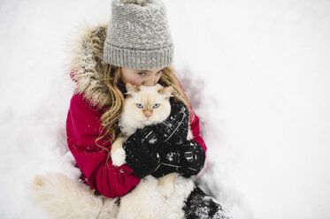 Porträt einer grünäugigen weißen Katze, die von einem Mädchen im Schnee umarmt wird - CUF05237