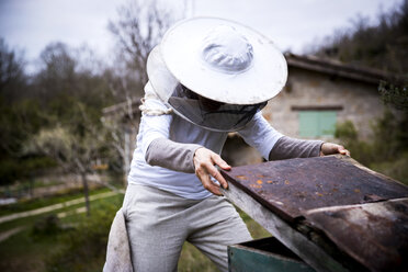 Imkerin beim Entfernen des Bienenstockdeckels im Garten - CUF05247