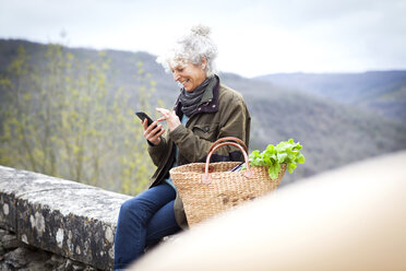 Woman sitting on wall texting on smartphone, Bruniquel, France - CUF05256