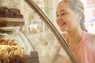 Mädchen in einer Bäckerei betrachtet lächelnd die Kuchen in der Vitrine - CUF05283