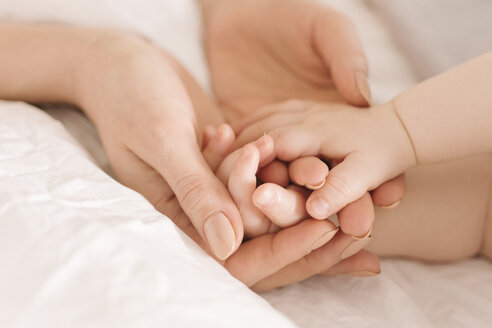 Mutter hält die Hände ihres Babys auf dem Bett - CUF05333