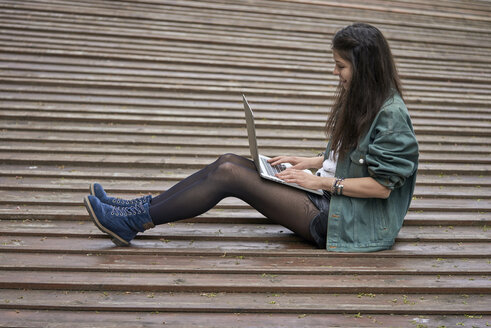 Junge Frau sitzt im Freien auf dem Boden und benutzt einen Laptop - BEF00044