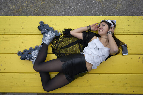 Smiling woman with inline skates lying on yellow table stock photo