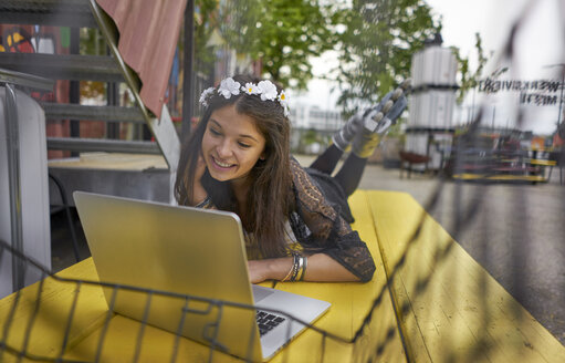 Lächelnde Frau mit Inline-Skates, die auf einem gelben Tisch liegt und einen Laptop benutzt - BEF00047