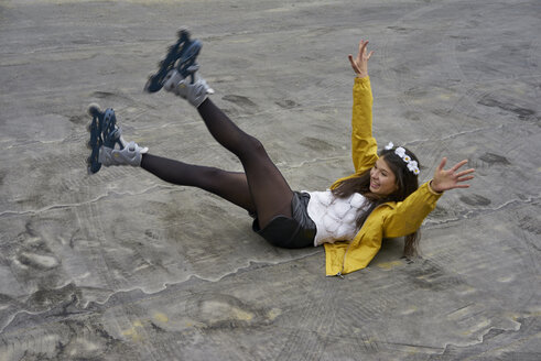 Smiling woman with inline skates falling on ground - BEF00048