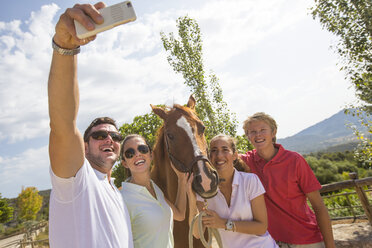 Bräutigam und Freunde machen Smartphone-Selfie mit Pferd in einem ländlichen Stall - CUF05414