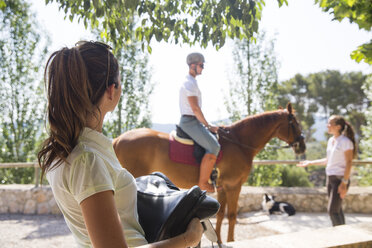 Pferdepflegerin trägt Sattel in einem ländlichen Stall - CUF05418