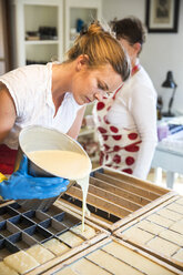 Junge Frau gießt in einer Werkstatt für handgemachte Seife flüssige Lavendelseife in Formen - CUF05431