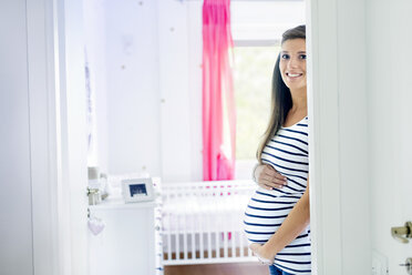 Porträt einer schwangeren Frau im Kinderzimmer, die lächelnd in die Kamera schaut - CUF05453